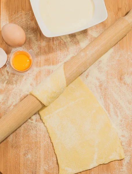 Homemade raw dough with flour and eggs placed on a wooden table with a rolling pin.