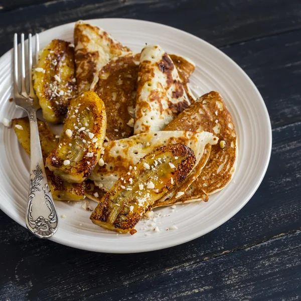 Pancake with honey and almonds and fried bananas on a ceramic plate on a dark wooden background. Delicious breakfast or snack