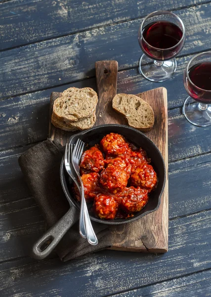 Meatballs in a pan and two glasses of red wine on rustic wooden board