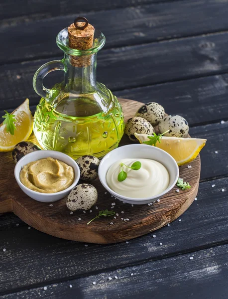 Mayonnaise and ingredients for cooking - olive oil, quail eggs. lemon, mustard and spices on wooden background