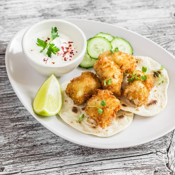 Crispy fried fish on a homemade tortilla on a light wooden background