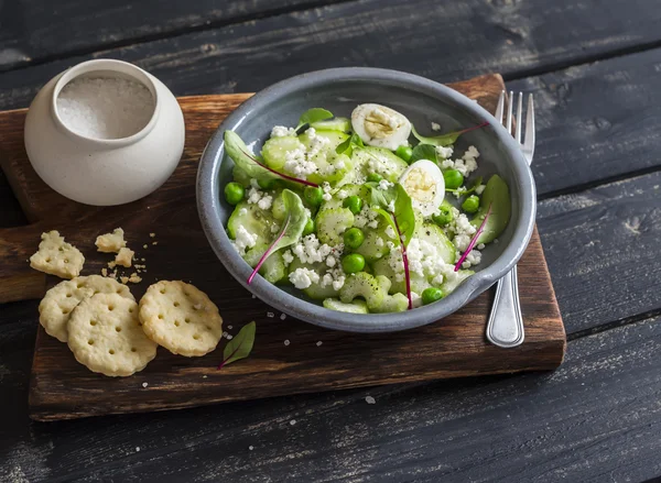 Healthy breakfast or snack - salad with cucumber, celery, quail eggs and cheese and homemade savoury cheese biscuits on a wooden rustic board on a dark background