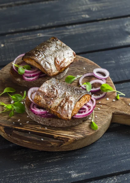 Sandwiches with grilled fish and quick pickled onions on rustic wooden board