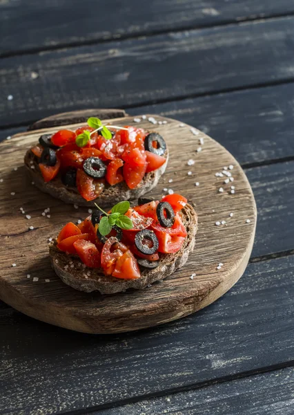 Tomato and olive bruschetta on rustic wooden board. Healthy delicious snack or appetizer with wine