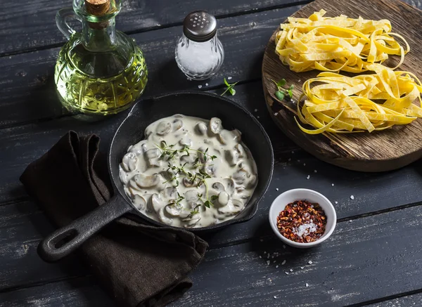 Ingredients for cooking pasta with creamy mushroom sauce - dry pasta, mushroom cream sauce, olive oil and spices. On a dark wooden background. Healthy delicious food
