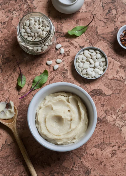 Bean puree in a ceramic bowl, jar with raw beans on a stone background. Top view