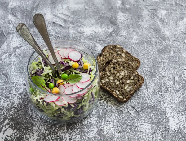 Fresh vegetable salad with white and red cabbage, cucumber, radish and cilantro in a glass jar on a stone texture. Healthy vegetarian food.