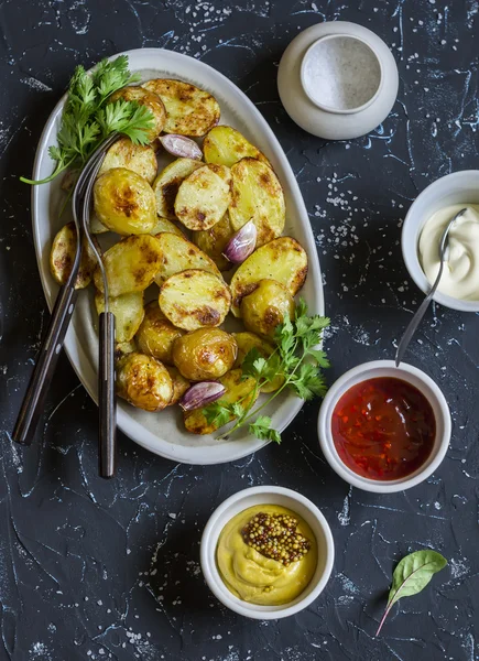 Baked potatoes and sauce him - homemade mayonnaise, ketchup and mustard. Delicious lunch or snack. On dark stone background