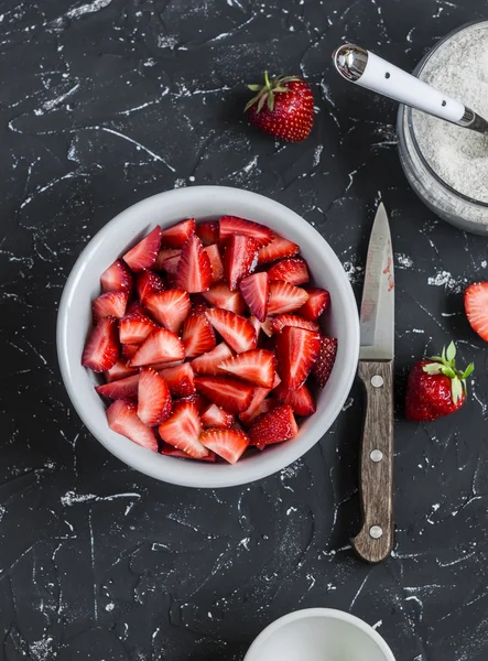 Chopped strawberries and the jar with whole grain flour on a dark stone background. Ingredients for making strawberry pie