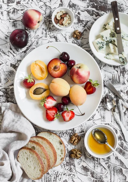 Summer fruits - apricots, peaches, plums, cherries, strawberries and blue cheese, honey, walnuts, bread on a light stone background. Healthy, diet, vegetarian food. Delicious summer dessert, breakfast  or snack