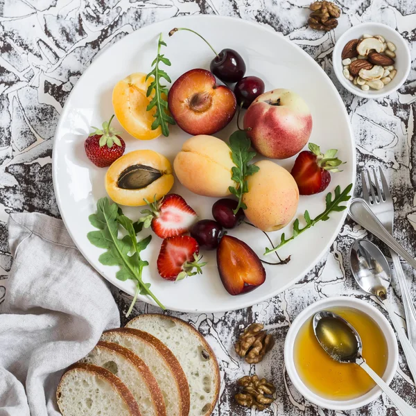 Summer fruits - apricots, peaches, plums, cherries, strawberries and  honey, walnuts on a light stone background