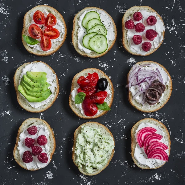 Variety of sandwiches - sandwiches with cheese, tomatoes, anchovies, roasted peppers, raspberries, avocado, bean pate, cucumber, olives. On a blue background, top view.
