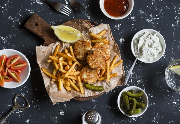 Fish balls, potato chips, pickles cucumber, tomatoes, sauces on a dark background. Top view
