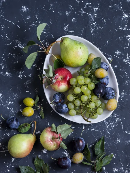 Fresh fruit - grapes, pears, apples, plums on a dark background, top view