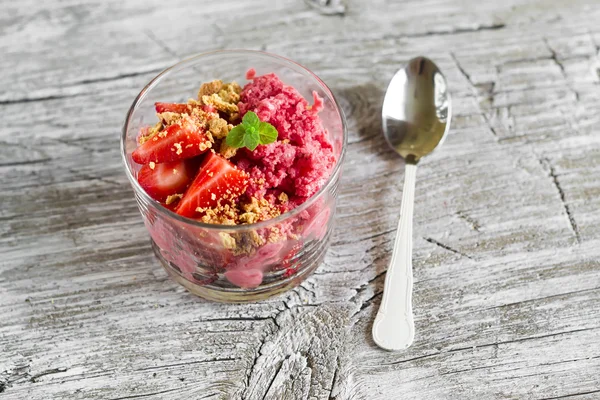 Frozen yogurt with strawberries and cookie crumbs in a glass bowl