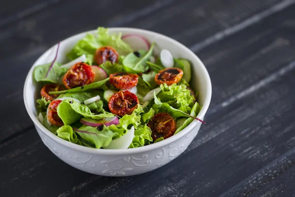 Salad with fresh vegetables, garden herbs and sun-dried tomatoes in a white bowl