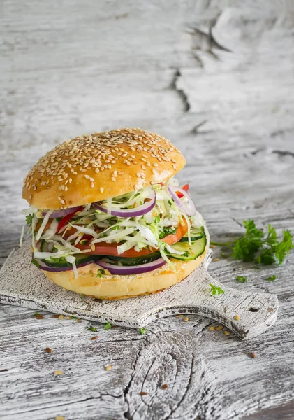 Delicious veggie burger with cabbage, tomato, cucumber, onions and peppers on a light wooden surface