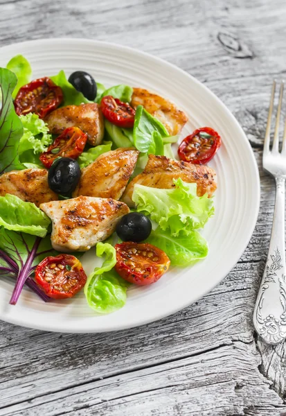 Fresh salad with chicken breast, sun-dried tomatoes, green salad and olives on a white plate