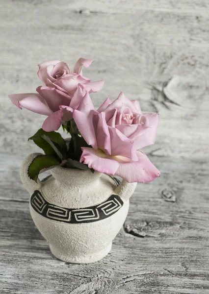 Pink roses in a ceramic vase with Greek ornament on a white wooden surface