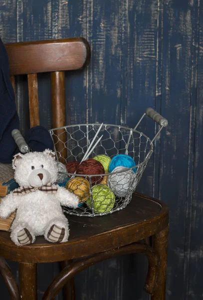 Basket with wool yarn and knitting, books and a toy bear on the old chair