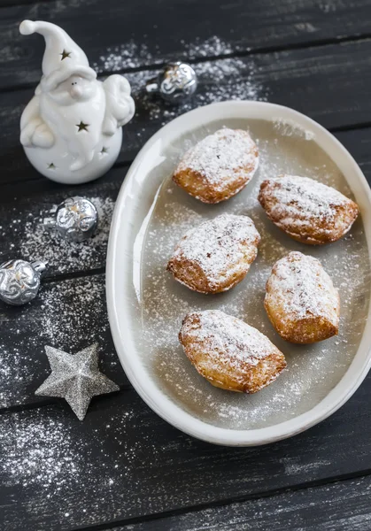 Cookies madeleines with powdered sugar on the oval plate, ceramic Santa Claus and Christmas decorations