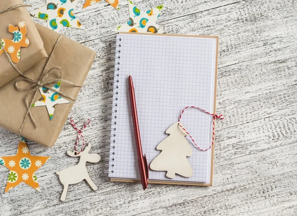 Christmas gifts, Christmas ornaments and an open blank notebook on a light wooden table