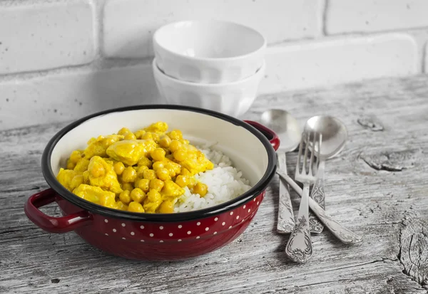 Chicken curry with chickpeas and rice in a vintage enamel bowl on bright wooden surface