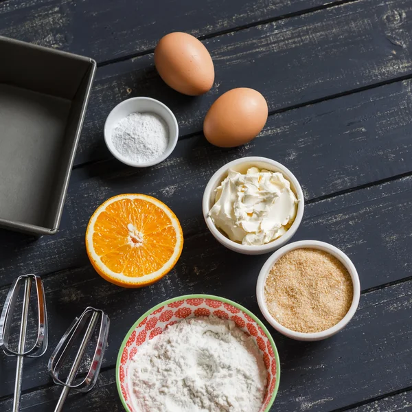 Ingredients for baking. raw ingredients - flour, eggs, butter, sugar, orange - to cook orange cake. Ingredients for the dough. On a dark wooden surface