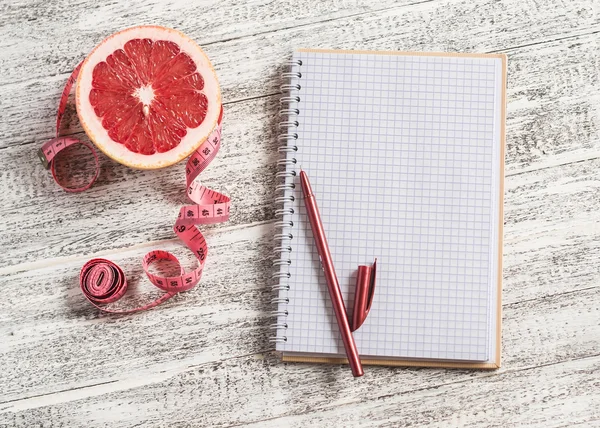 Open a blank Notepad, grapefruit and measuring tape on a light wooden table. The concept of healthy nutrition, diets, healthy lifestyle. Free space for text