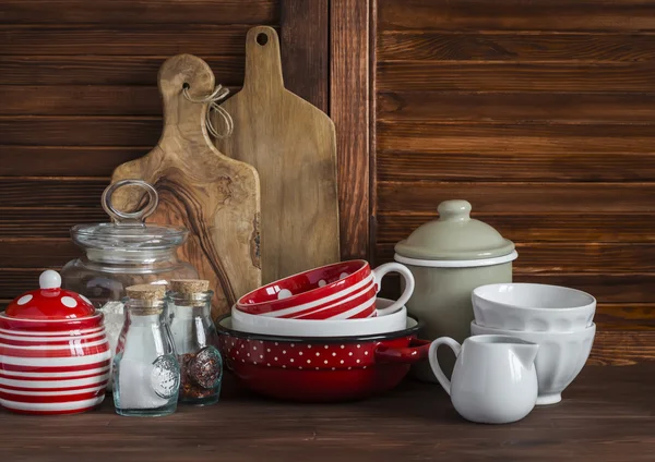 Rustic kitchen still life. Olive cutting board,  jar of flour,  bowls, pan, enamelled  jar,  gravy boat. On a dark brown wooden table. Vintage and rustic style