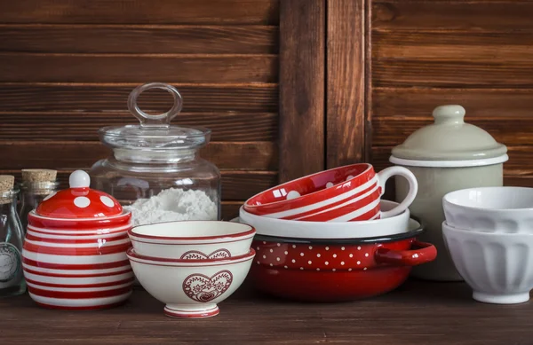 Kitchen still life. Vintage crockery - jar of flour, ceramic bowls, pan, enamelled  jar,  gravy boat. On a dark brown wooden table. Vintage and rustic style