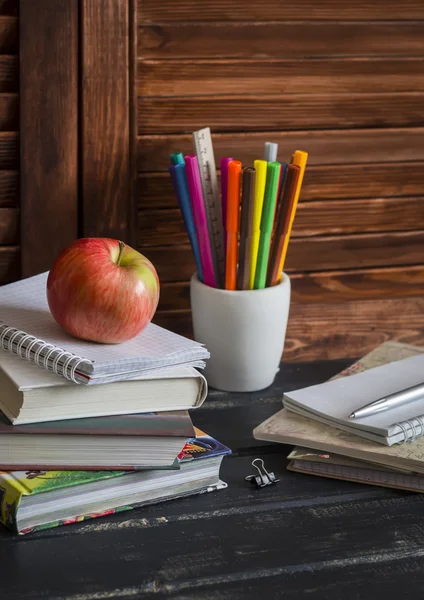 Schoolchild and student studies accessories. Books, notebooks, notepads, colored pencils, pens, rulers and a fresh red apple. Homemade baby desktop. The concept of education and training
