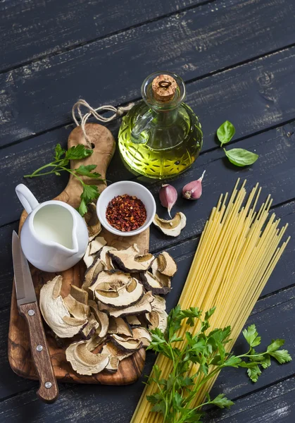 Raw ingredients for cooking pasta with porcini mushrooms - dried porcini mushrooms, spaghetti, cream, garlic, parsley, basil, olive oil and spices. On white wooden table. Vegetarian lunch. Healthy food