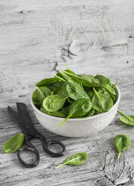 Fresh baby spinach in a white bowl on light rustic wooden board