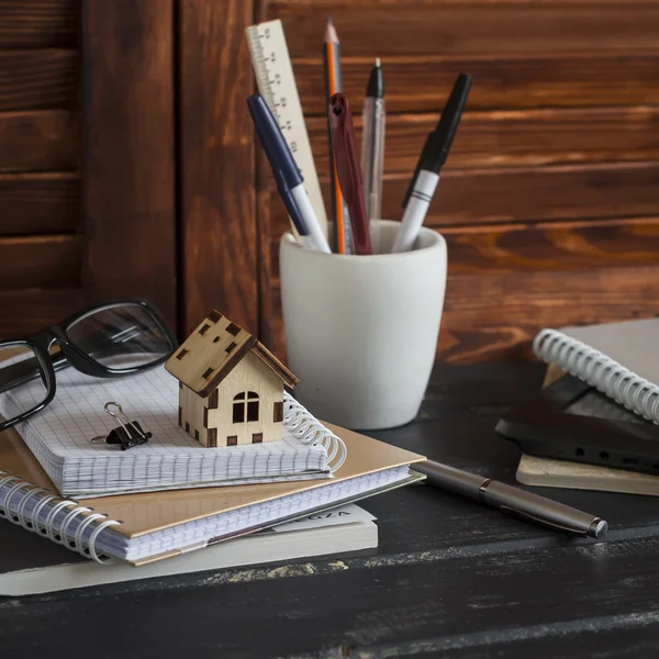Workplace designer and architect with business objects - books, notebooks, pens, pencils, rulers, tablet, glasses and a model of a wooden house. Planning of the construction of a house.