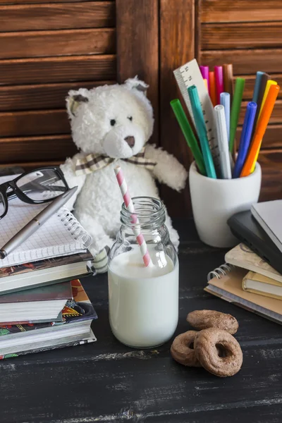 Child domestic work space and accessories for training and education - books, journals, notepads, notebooks, pens, pencils, tablet and toy bear, bottle of milk and biscuits.