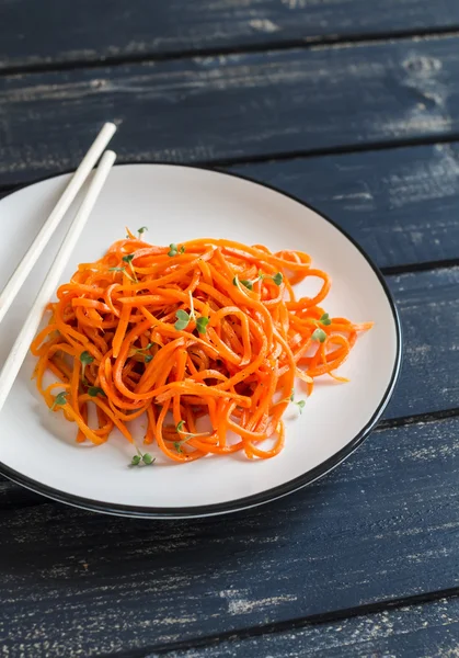 Spicy pickled carrot salad in an asian style on a white plate on a dark wooden background. Vegan food