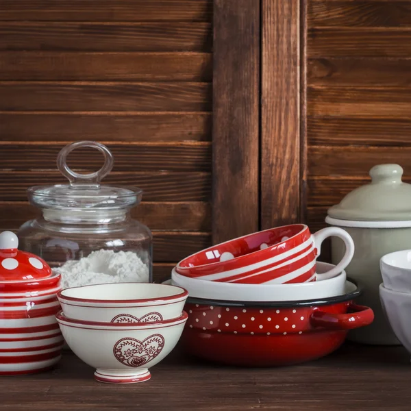 Kitchen still life. Vintage crockery - jar of flour, ceramic bowls, pan, enamelled  jar,  gravy boat. On a dark brown wooden table. Vintage and rustic style