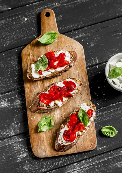 Open sandwich cheese, roasted red sweet peppers and basil on a dark wooden board