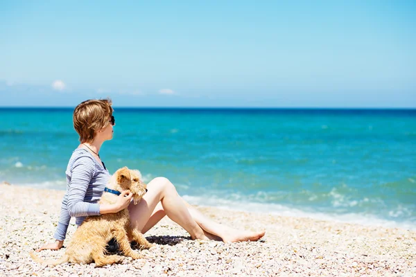 Beautiful girl sitting on the beach with a terrier dog