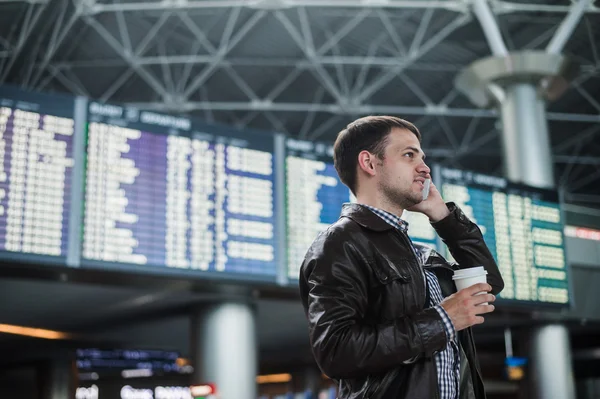 Smiling young traveller man at the airport talking on phone in front of timetable board