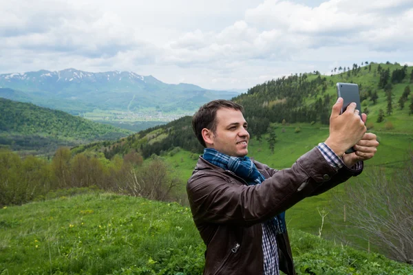 Happy young man smiling and making selfies holding tablet PC in the mountains