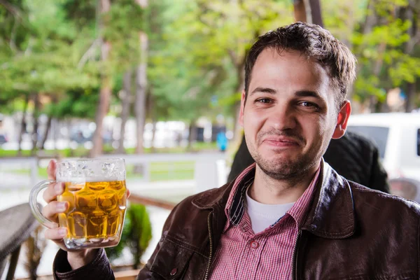 Man drinking beer outdoors in a cafe with funny expressions