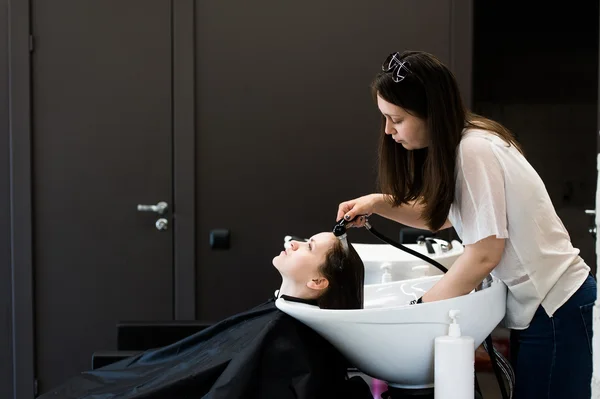 Young female stylist drying woman hair with water in salon barbershop