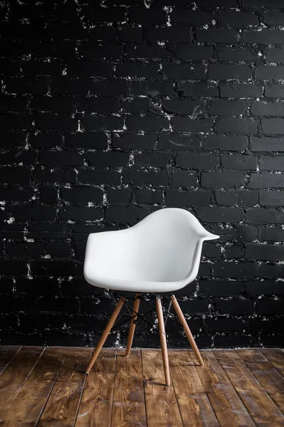 White chair standing in room on brown wooden floor over black brick wall