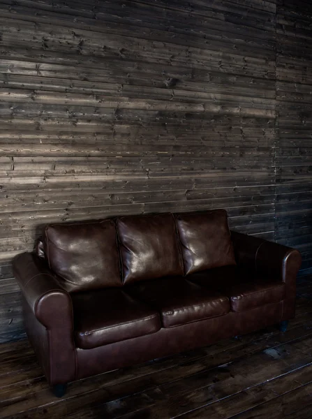 Vintage brown leather sofa on a wooden wall and floor