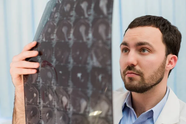 Closeup portrait of intellectual man healthcare personnel with white labcoat, looking at brain x-ray radiographic image, ct scan, mri, clinic office background. Radiology department