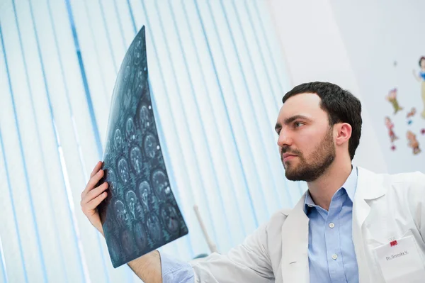 Closeup portrait of intellectual man healthcare personnel with white labcoat, looking at brain x-ray radiographic image, ct scan, mri, clinic office background. Radiology department