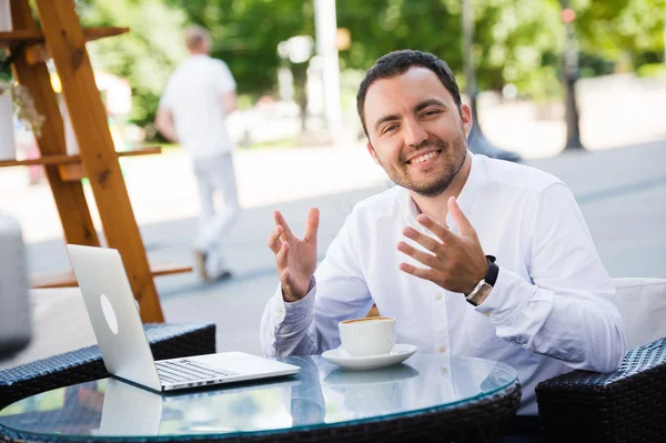 Young handsome man smiling and drinking coffee in a seaside restaurant. He is happy, looking at camera