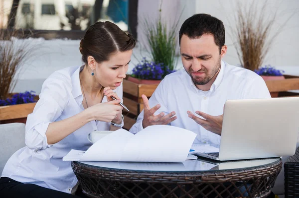 Male and female business colleagues working together on a hard problem at outdoors cafe. They have strained expression on their faces